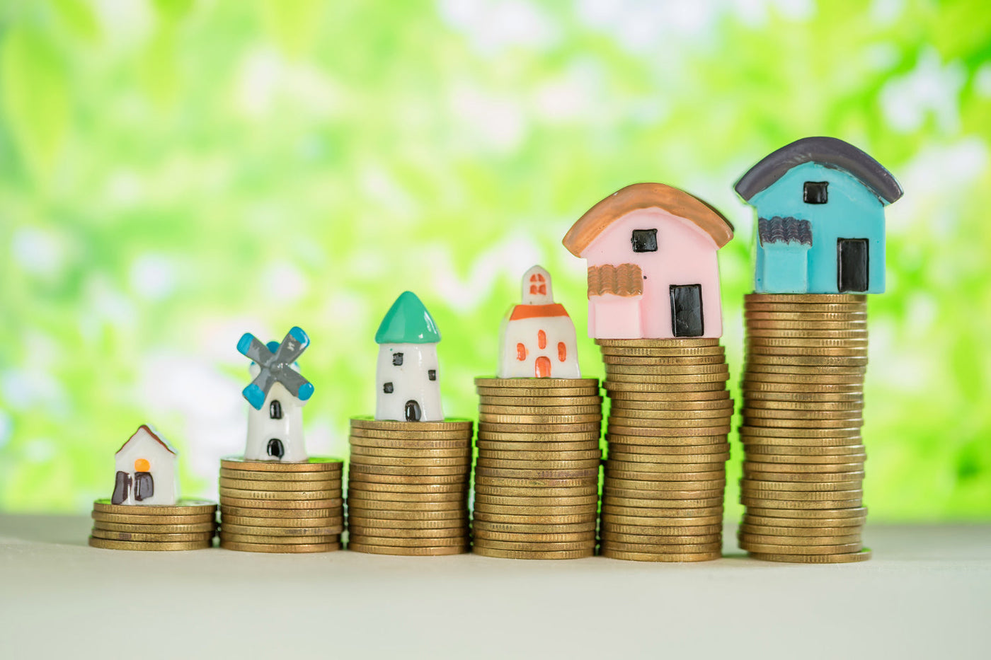 This image creatively represents real estate investment or property value growth. It features small model houses placed on stacks of coins, increasing in height, symbolizing financial growth or housing market trends.