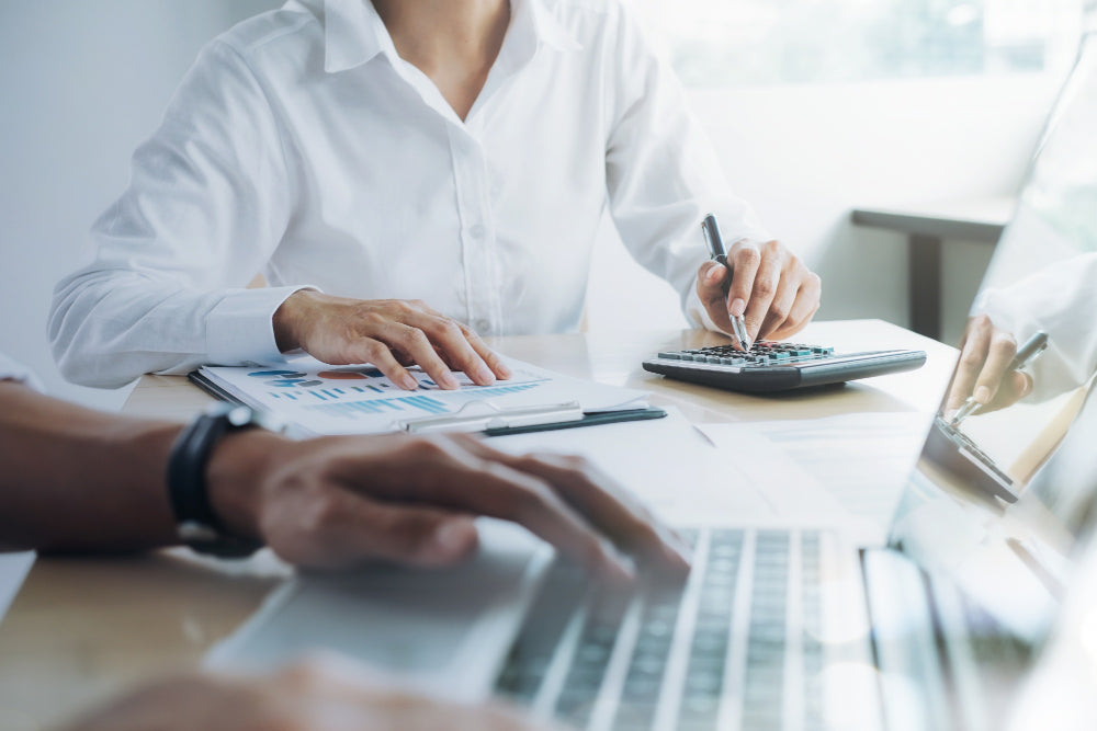 Business professionals working together at a desk with financial documents, a calculator, and a laptop, focusing on data analysis and calculations.