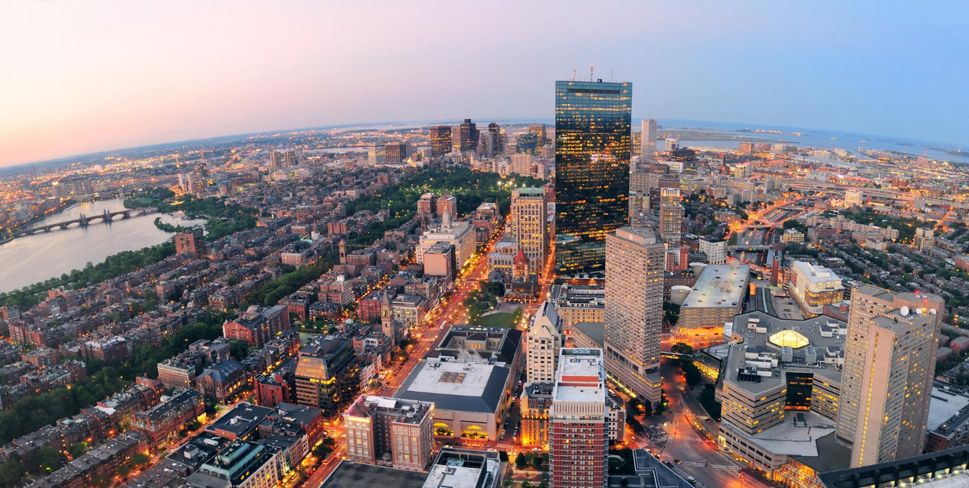 Aerial view of a city skyline at dusk, featuring illuminated streets, high-rise buildings, and a river with bridges, creating a vibrant urban landscape.