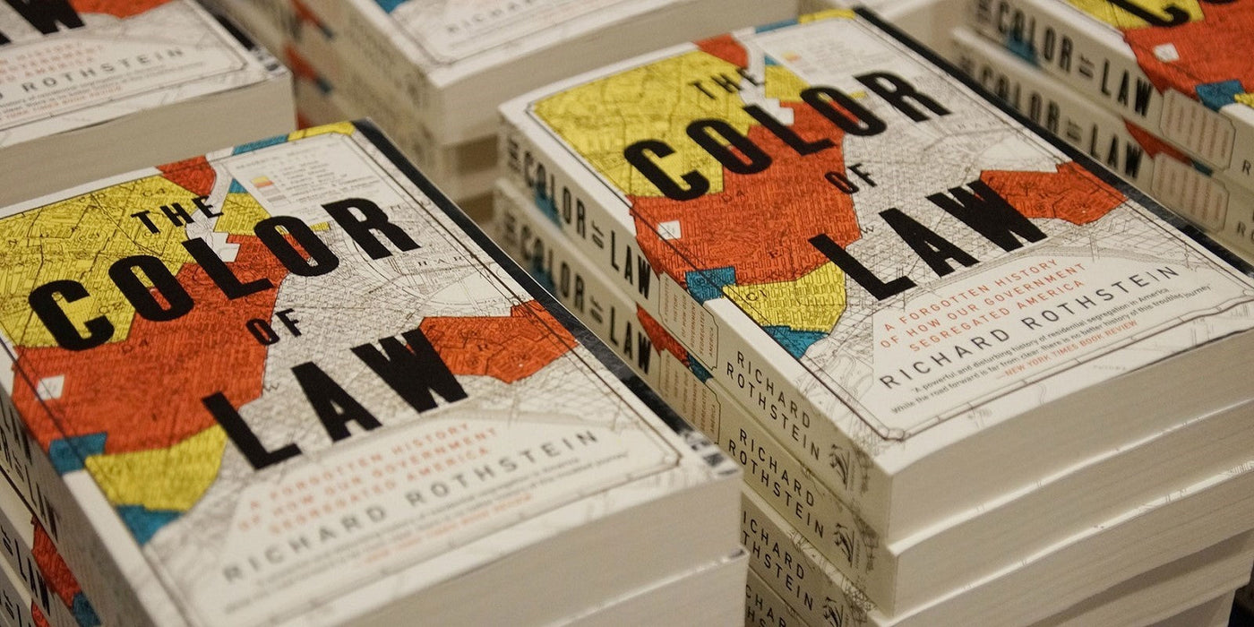 Stacks of the book 'The Color of Law' by Richard Rothstein, featuring a cover design with a red, yellow, and blue historical map, discussing government-driven racial segregation in America.