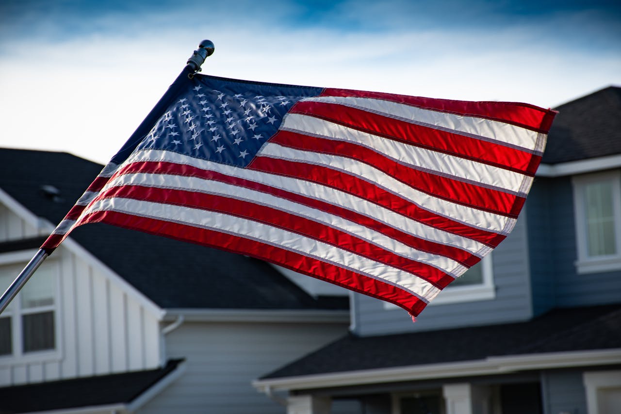 An American flag waving in the wind in front of a suburban house with a blue and white exterior.