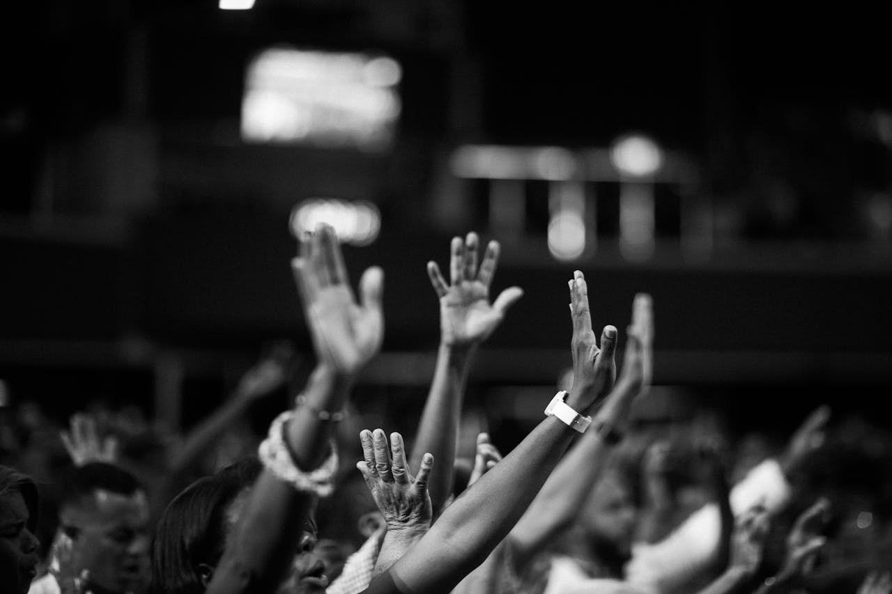 Black and white photo capturing a group of people raising their hands in unison during a gathering