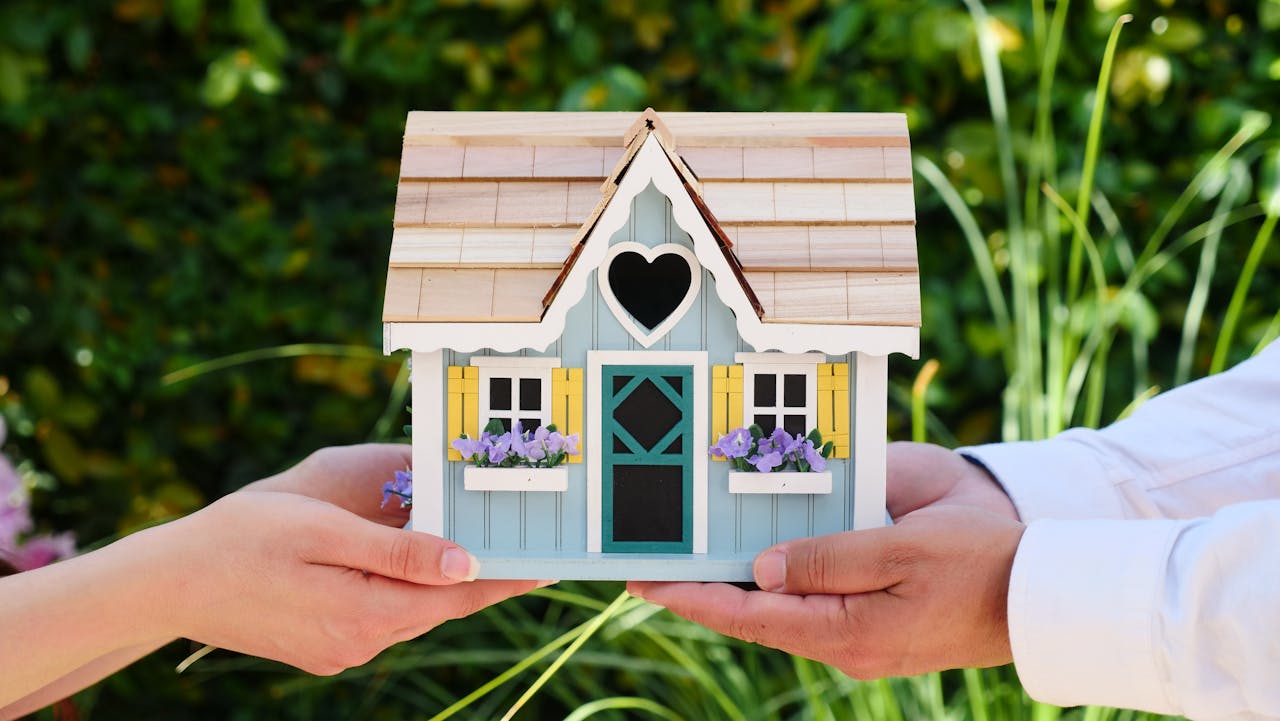 A miniature house with a charming design is held between two people, symbolizing homeownership, real estate, or partnership.