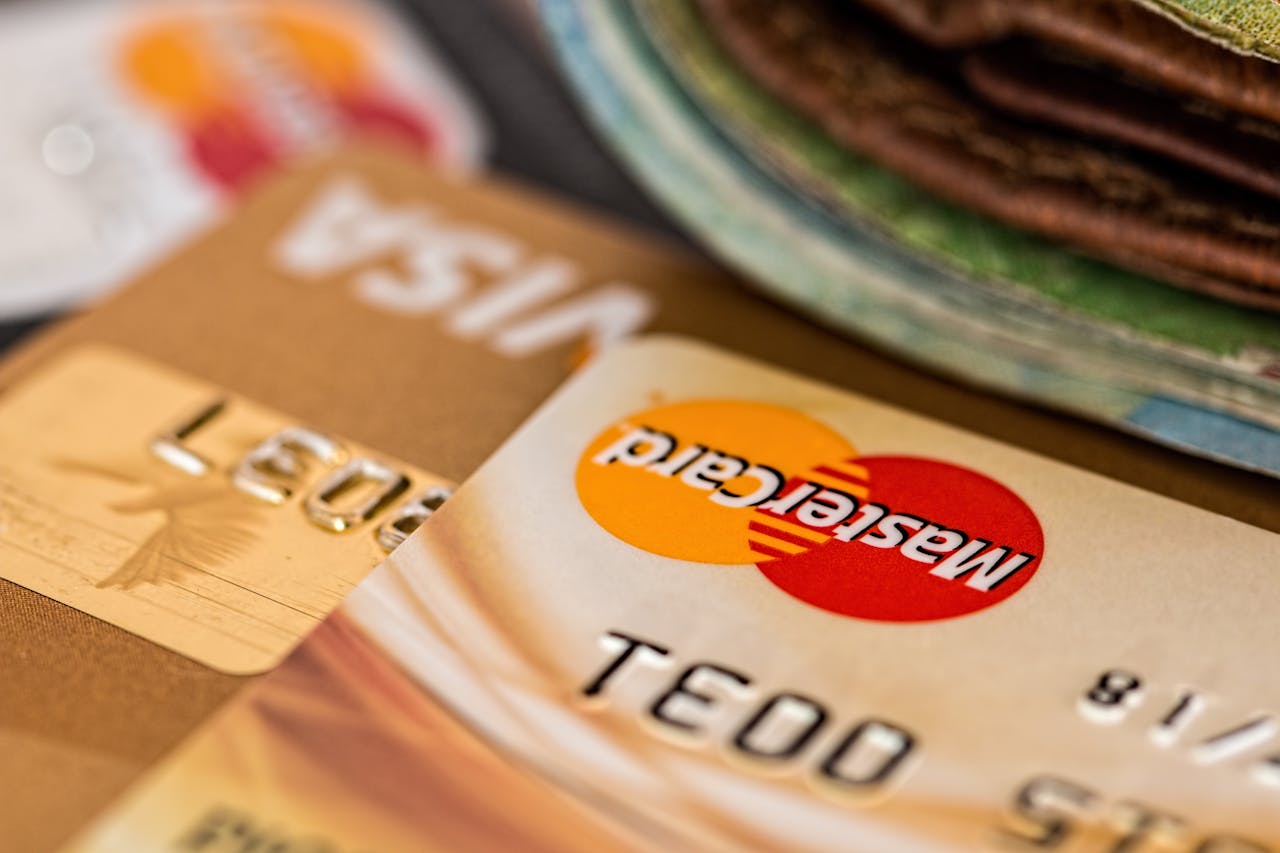 A close-up of multiple credit cards, including Mastercard and Visa, stacked on top of each other with a wallet in the background, symbolizing financial transactions, banking, or personal finance.