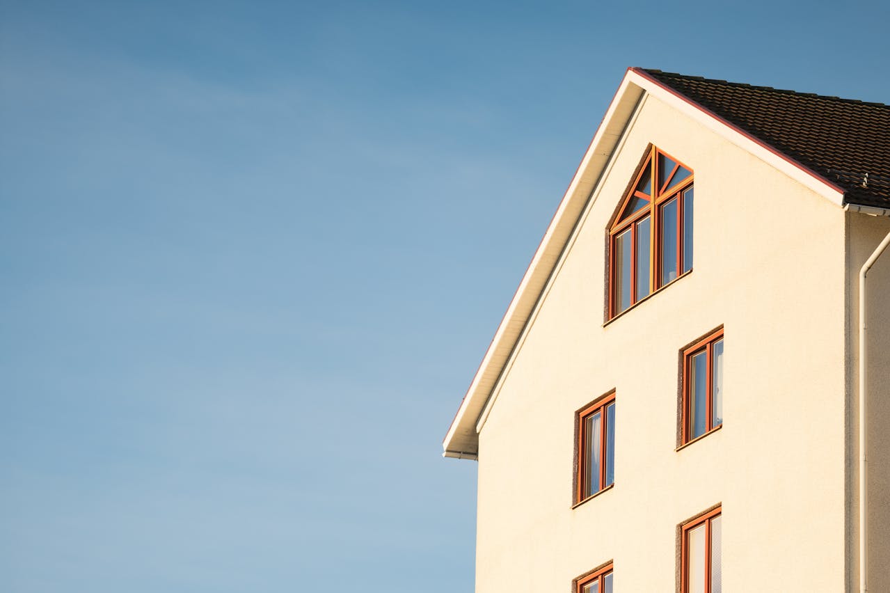 Minimalist view of a modern house with a beige facade and brown-framed windows against a clear blue sky, capturing a clean and architectural aesthetic.