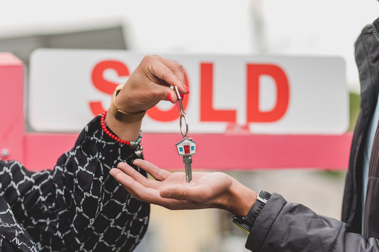 A home purchase moment, with keys being handed over in front of a "SOLD" sign.